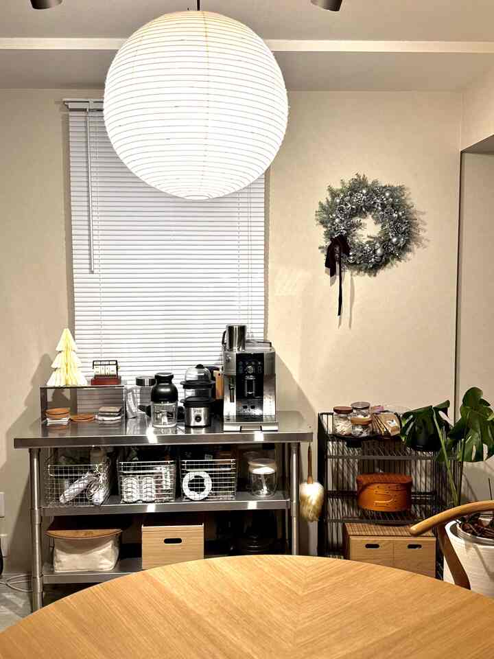 白い壁とブラインドを背景にした北欧風のキッチンスペース、ステンレス作業台とホームカフェ用のコーヒー機器が配置された清潔感のあるインテリア