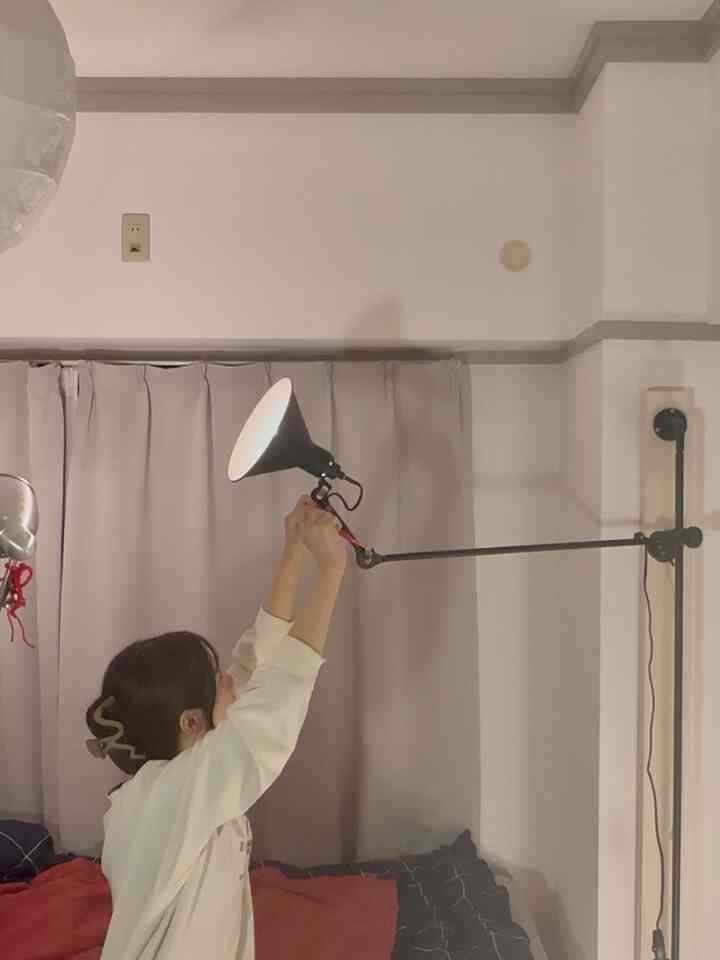 白い壁とベージュのカーテンがある狭い寝室、壁に取り付けられた黒い照明が機能的に配置された雰囲気のあるインテリア