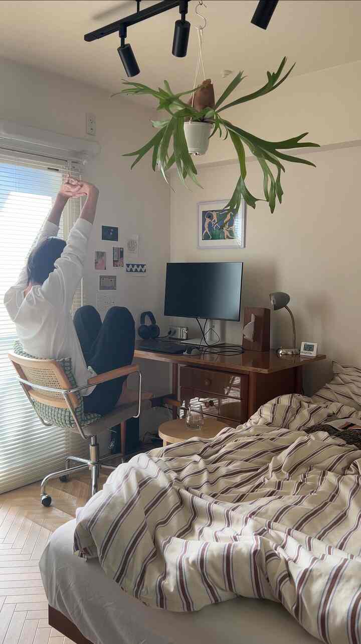 ナチュラルな色調の寝室兼ホームオフィス、木製デスクとオフィスチェア、ベッドカバーが配置されたくつろげる空間