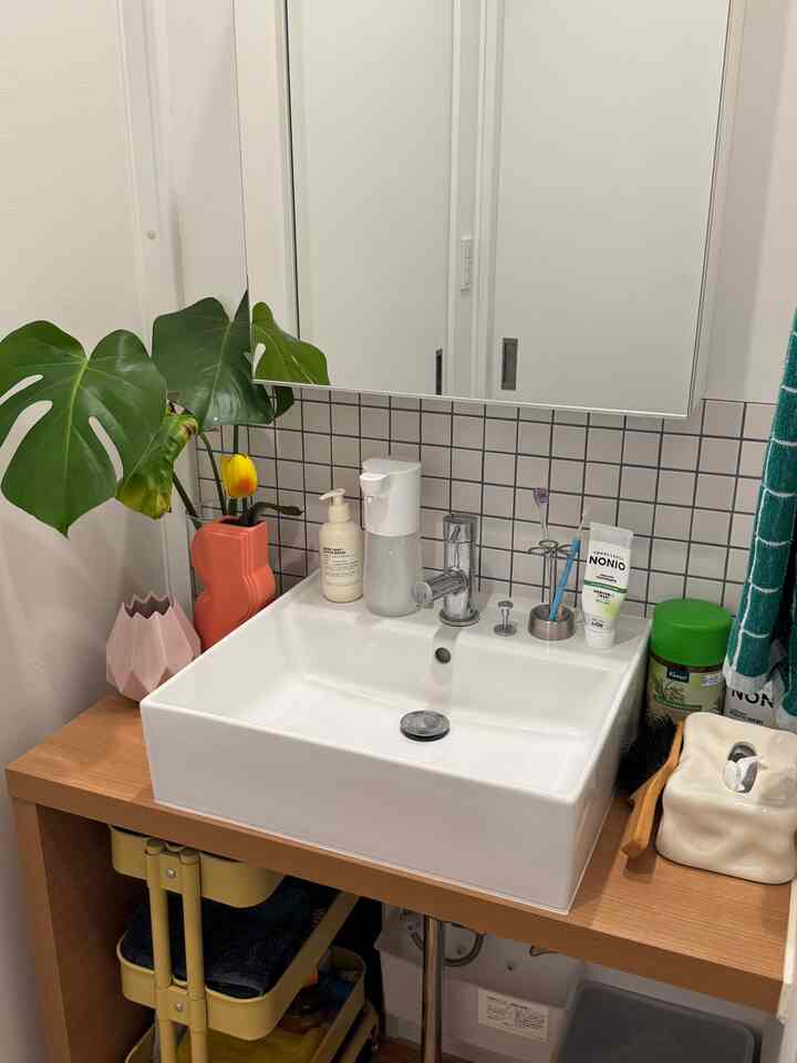 ナチュラルウッド調のカウンターとモザイクタイルの壁紙が配置されたバスルームの洗面台スペース