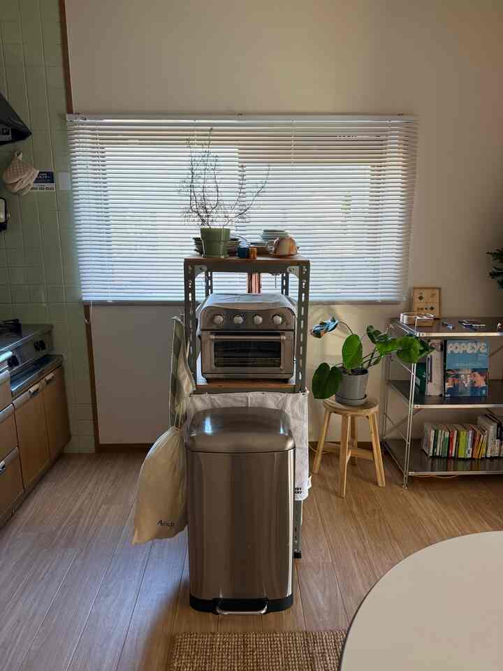 白とシルバーのトーンのキッチン、ステンレスのゴミ箱と収納棚、ブラインドが配置された印象的な空間