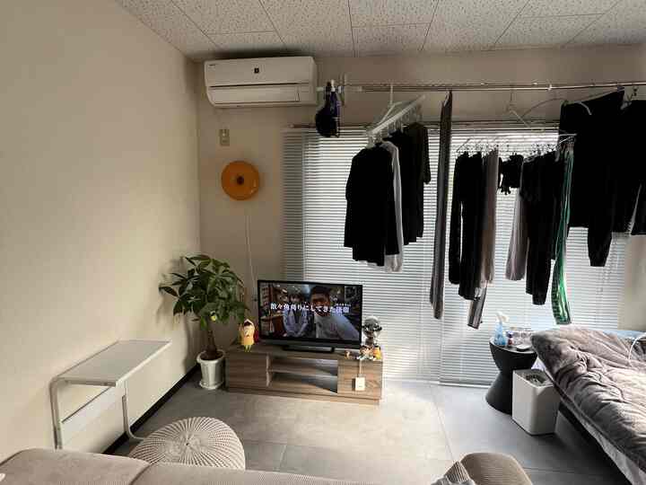 ベージュとナチュラルカラーのワンルームリビング、テレビ台とソファ、壁照明が配置された落ち着いた空間