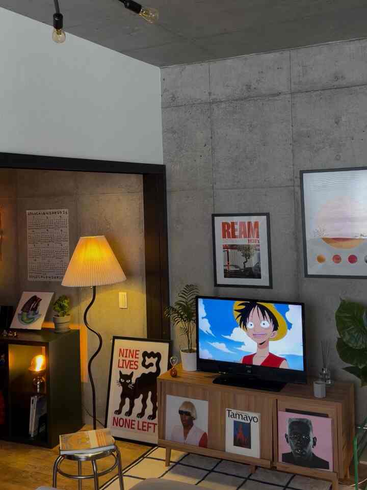 グレーのコンクリート壁と木目調のテレビ台があるインダストリアルなリビング、フロアランプと植物が配置された雰囲気のある空間