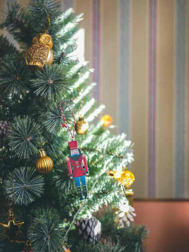 Green Christmas tree decorated with gold ornaments and warm string lights in a cozy setting