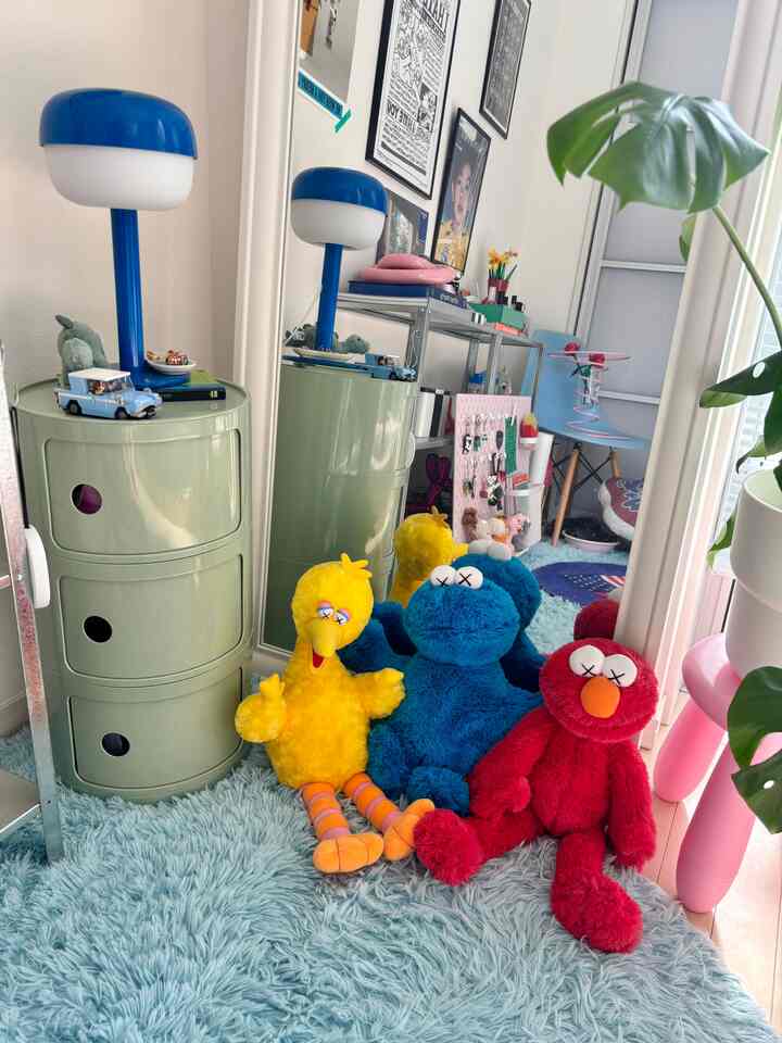 Pastel-toned 1LDK living space featuring colorful character plush toys, a blue shaggy rug, and modern storage furniture with cozy atmosphere