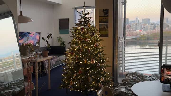 白い壁と黒いソファのあるリビング、中央にライトと飾りの付いたクリスマスツリーが配置された雰囲気のある空間