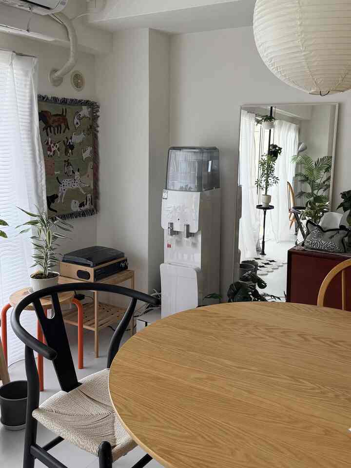 白と木目調の明るく清潔感のあるリビング、丸いダイニングテーブルと椅子、大きな鏡とペンダントライトが配置された雰囲気のある空間