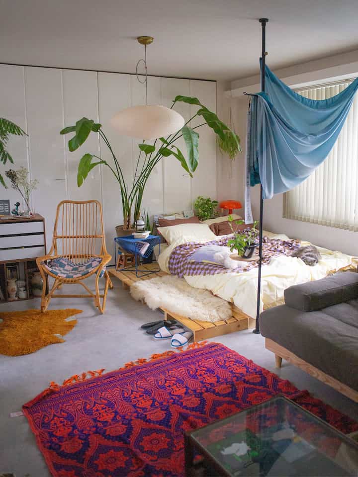 White and brown toned bedroom featuring a wide bed, rattan armchair, and plants in a natural modern interior