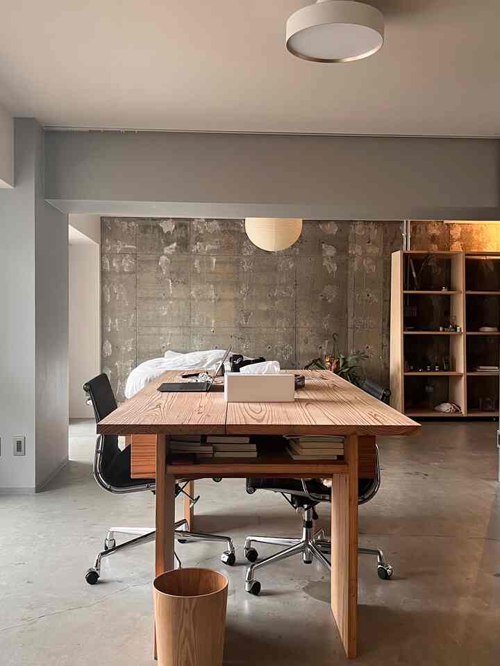 ナチュラルカラーとコンクリート壁が印象的なワンルーム、広い木製デスクとオフィスチェアが配置された実用的なワークスペース