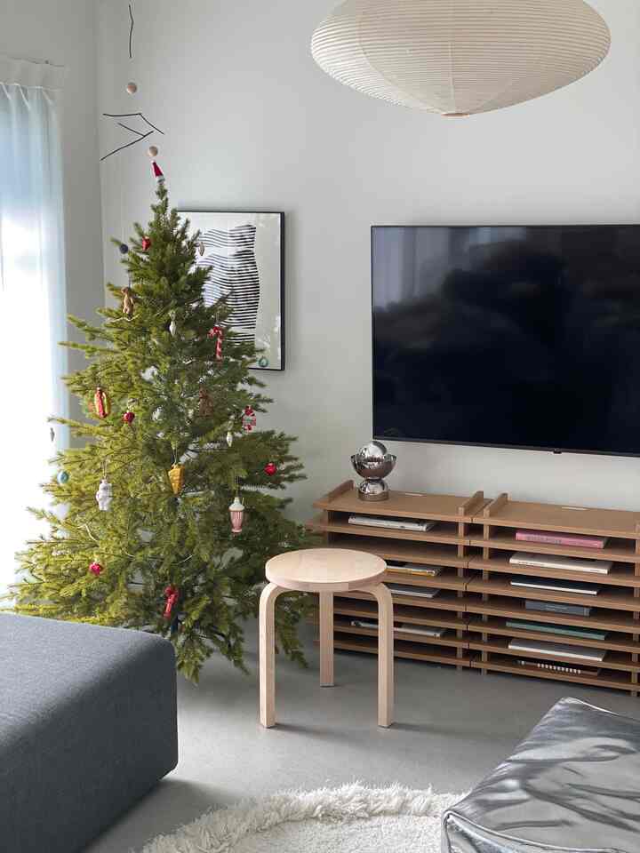 白い壁と天井のモダンなリビング、中央にナチュラルな木製スツールと緑色のクリスマスツリーが飾られた雰囲気あるインテリア