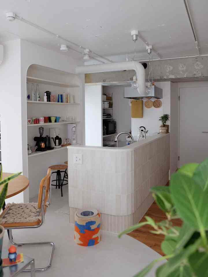 明るいホワイトとナチュラルウッドトーンのキッチン空間、多目的棚と木製のダイニングチェアが配置された雰囲気あるインテリア