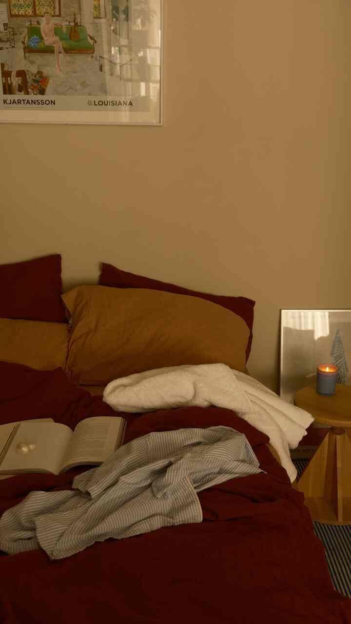 A beige-toned bedroom featuring a wooden side table, rust-colored bedspread, and a white waffle towel creating a cozy atmosphere
