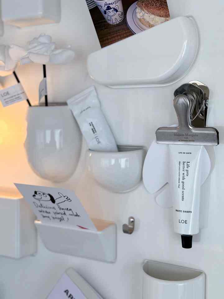 Minimal wall-mounted white storage holders and hand cream arranged on a clean white wall