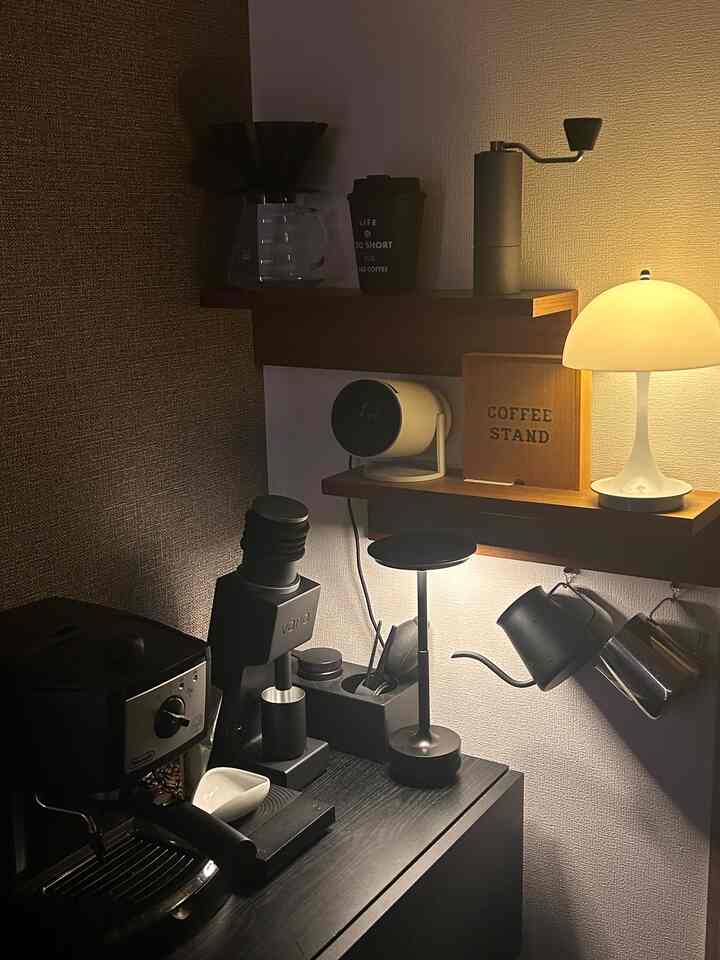 ダークブラウンの木目調と黒い家電が調和したワンルームのホームカフェコーナー、暖かい照明で雰囲気ある空間