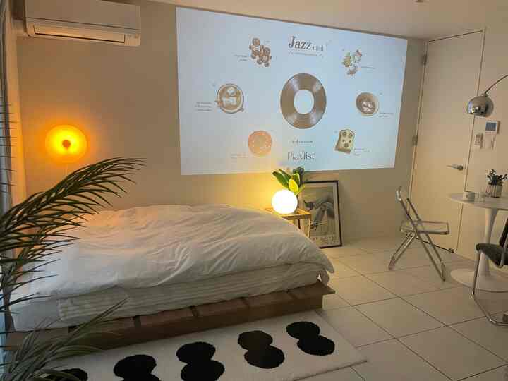 白い壁と床、茶色の木製ベッドフレーム、暖かい間接照明があるモダンでシンプルな一人用寝室のインテリア