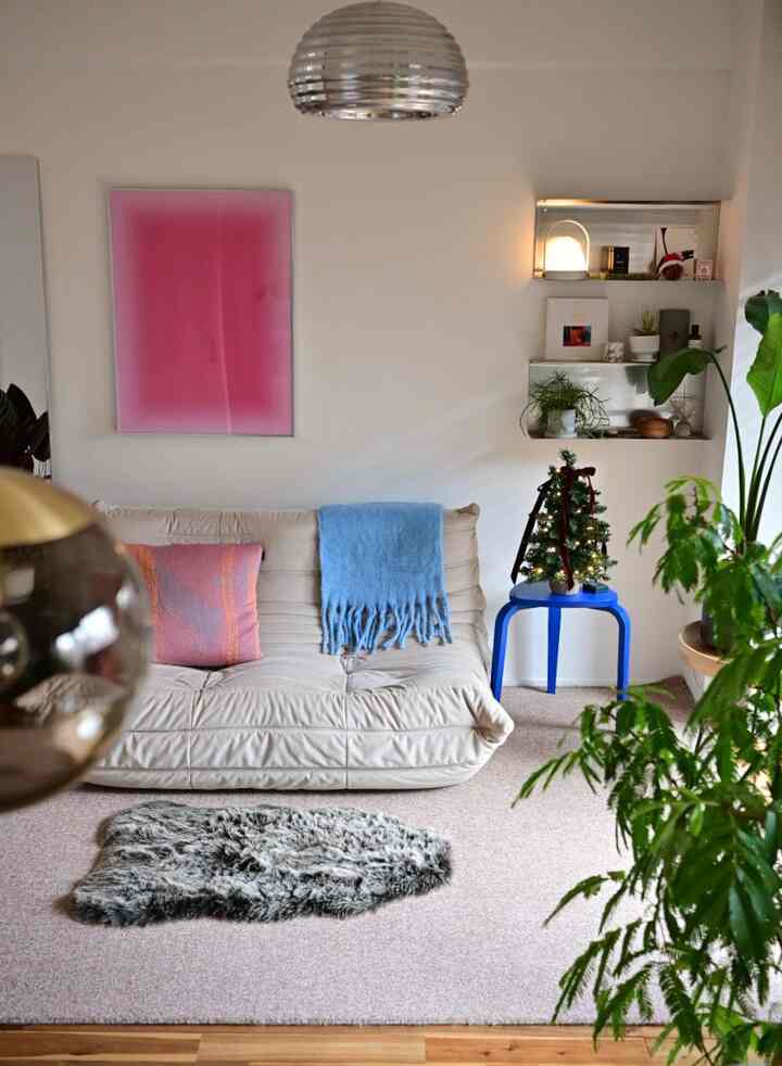 ベージュのソファに青いブランケット、ピンクの壁ポスターが配置されたミニマルな印象のリビング