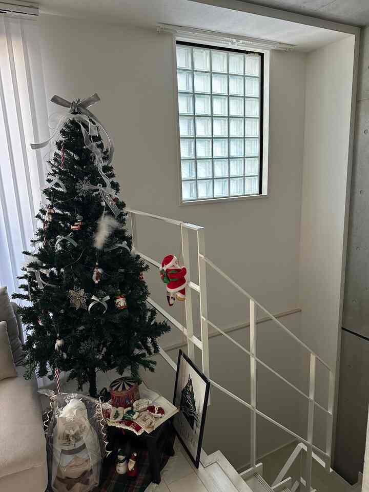 白い壁と階段のそばにリボン飾りのある緑のクリスマスツリーが配置された1LDKのリビングルーム