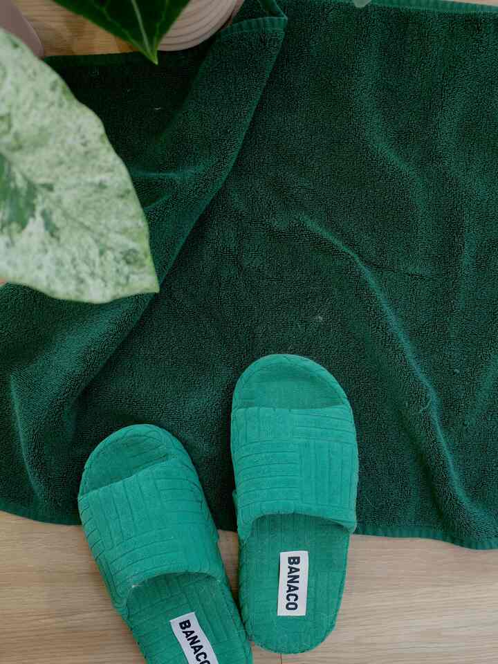Vivid green slippers and bath mat laid on a green-toned floor, showing textured fabric with visible pet hair