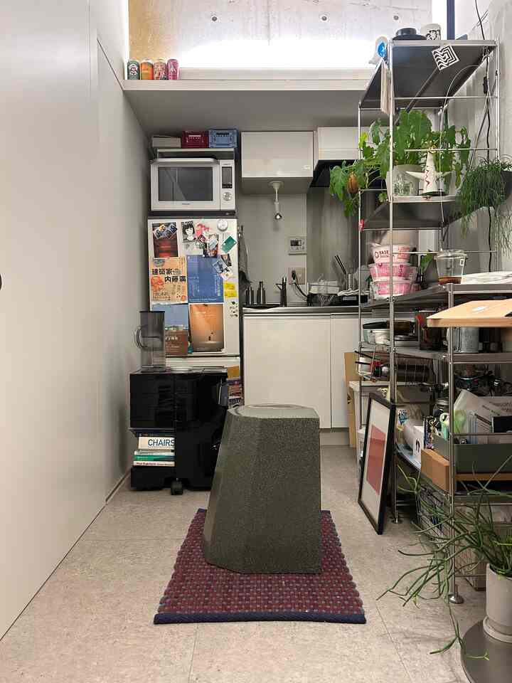Natural color dominated small kitchen space featuring an Arnold Circus Stool on a red rug amid clutter and metal shelving