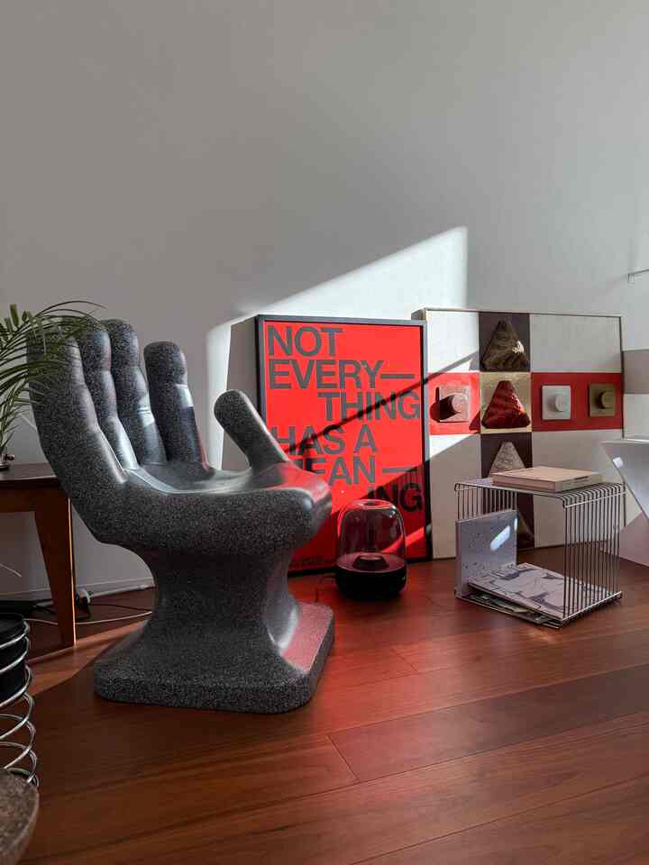 温かみのある木目調の床と黒のミッドセンチュリーモダンのハンドチェア、印象的な赤いポスターがある雰囲気の良いリビングスペース