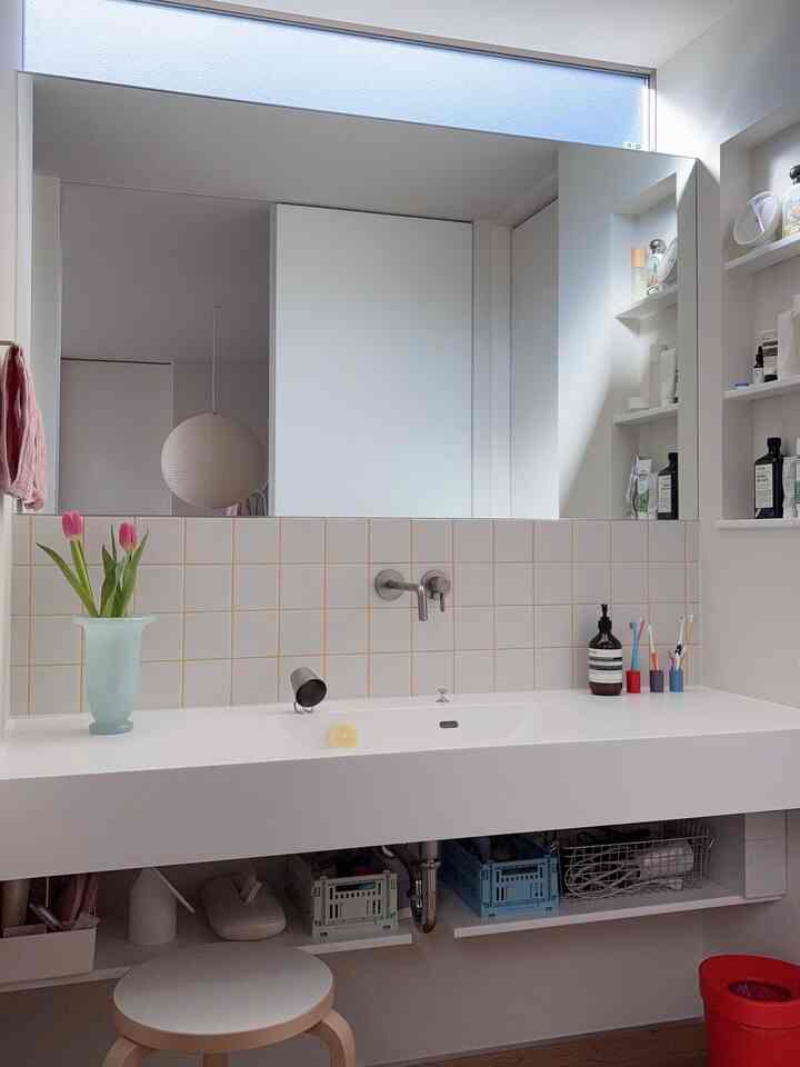 White-tone bathroom with tiled wall, stool, and natural light creating a minimal atmosphere