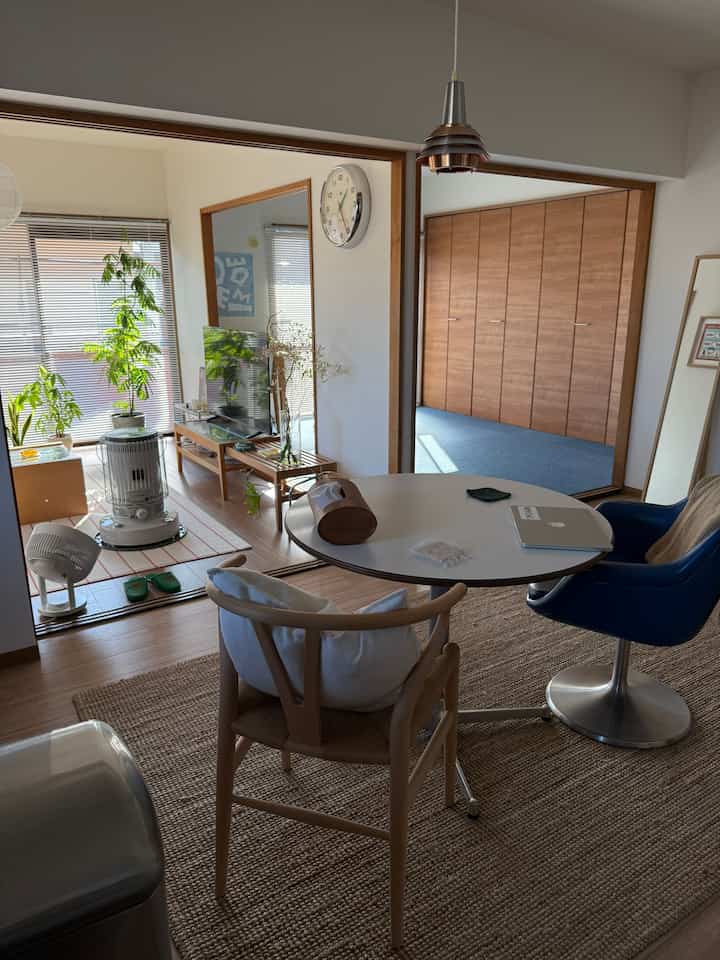 Natural wood tone and white-walled living room featuring round dining table, chairs, and a stand heater creating a cozy atmosphere
