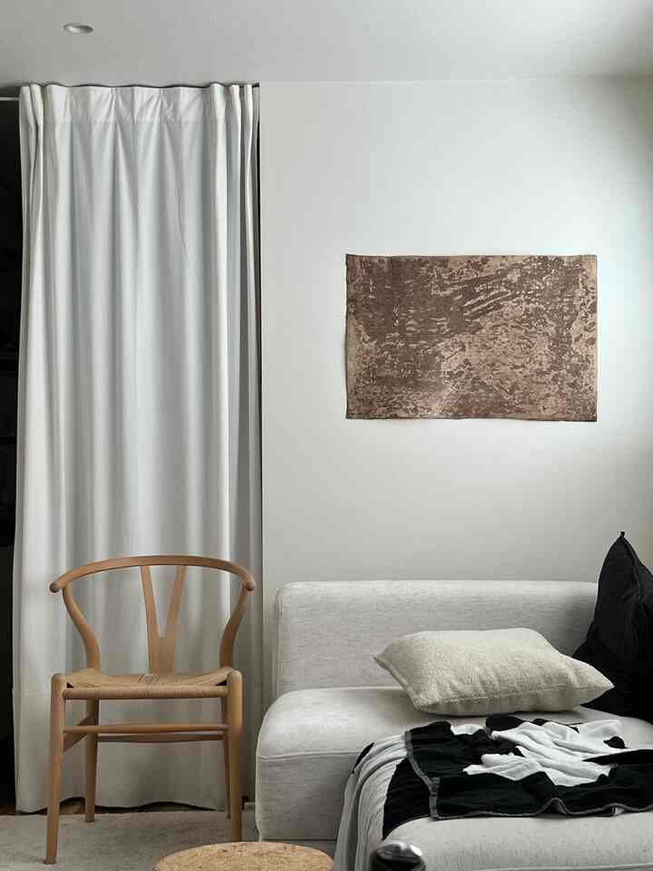 白と木目調が調和したワンルーム、カーテンとコーナーソファ、Yチェアが配置されたシンプルで自然な雰囲気のインテリア