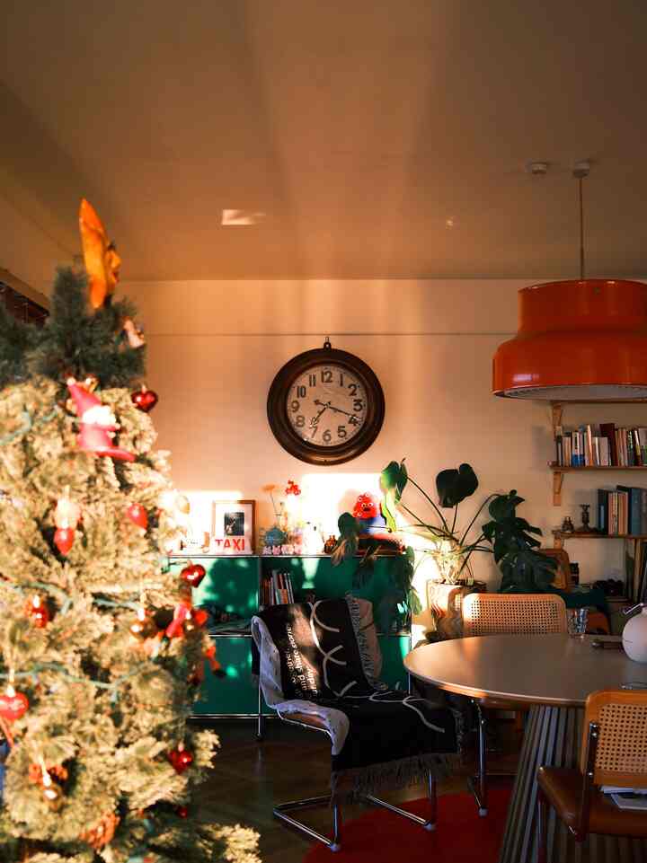 Warm-toned living room with green cabinet, orange pendant light, dining table, and a decorated Christmas tree