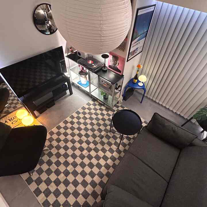 モノトーンとインダストリアルの雰囲気がある6畳のリビング、ソファベッドとチェッカーパターンのラグが配置された印象的な空間