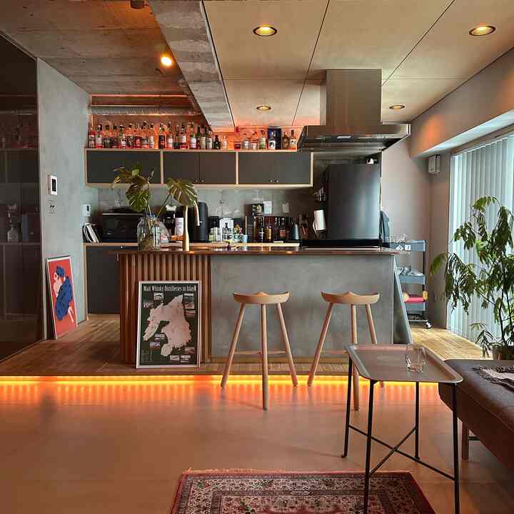 モダンでインダストリアルな雰囲気のキッチン兼ホームバー空間、木製のバースツールとブラインドが配置された印象的なインテリア