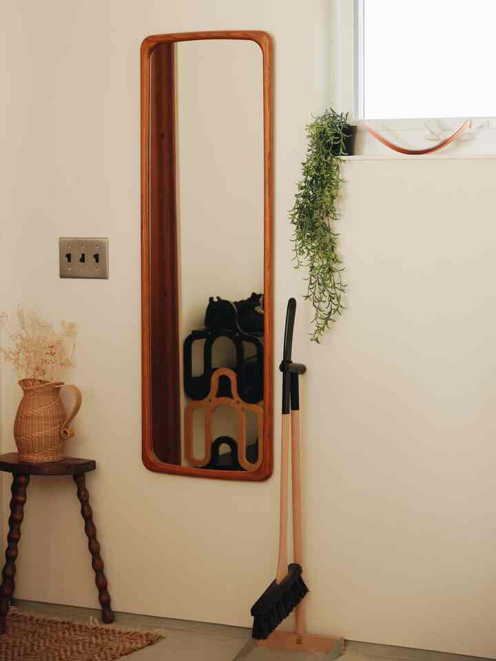 ベージュの壁に木製フレームの鏡と掃除道具が置かれた、ナチュラルな色調の北欧ヴィンテージ風玄関