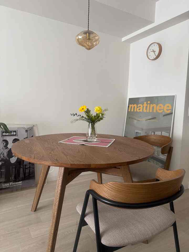 White-walled dining room with wood-tone round table, transparent vase with yellow flowers, simple and natural atmosphere