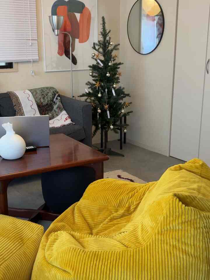 白とナチュラルトーンのリビング、黄色のビーンバッグとグレーのソファ、クリスマスツリーが配置されたシンプルな空間