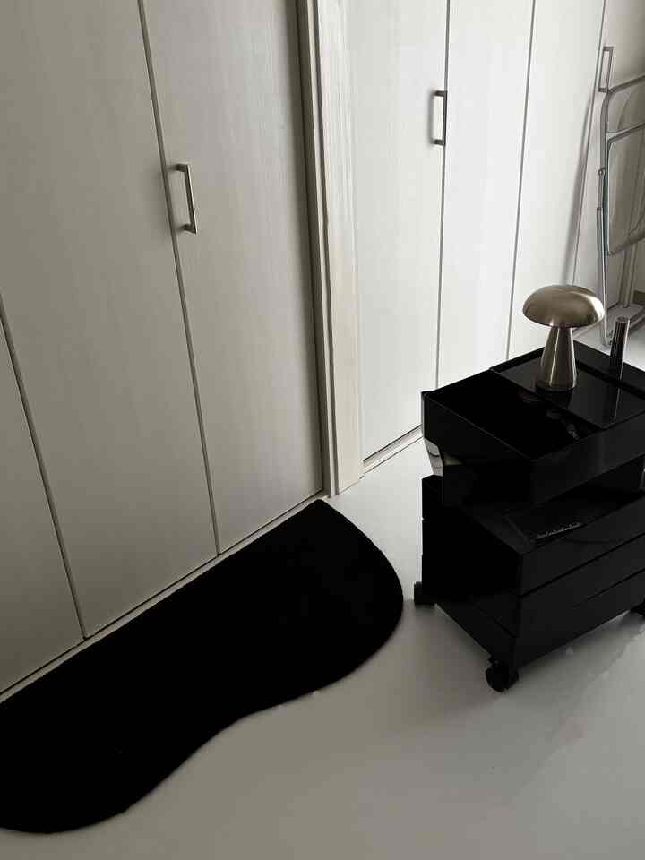 Monotone studio apartment with white floor and walls featuring a black kitchen cart and black rug