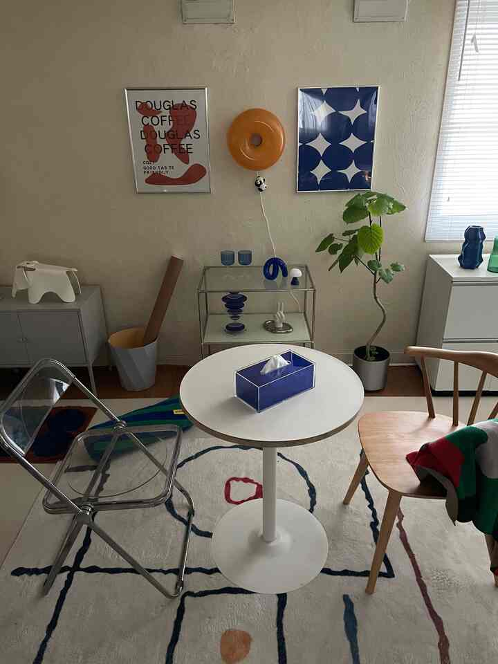 ホワイトとブルーの色調のリビング、丸テーブルと透明な椅子、植物が配置された印象的なミッドセンチュリーモダンのインテリア