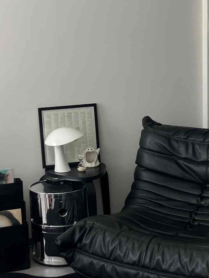 黒いレザーソファと白い壁、照明が配置されたモダンでシンプルなリビングの一角