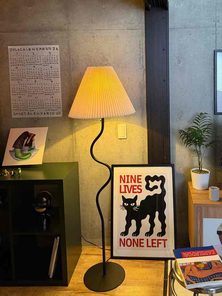 木目調の床とコンクリート壁が調和する空間に黒いフロアランプとアートポスターが配置された雰囲気のあるインテリア