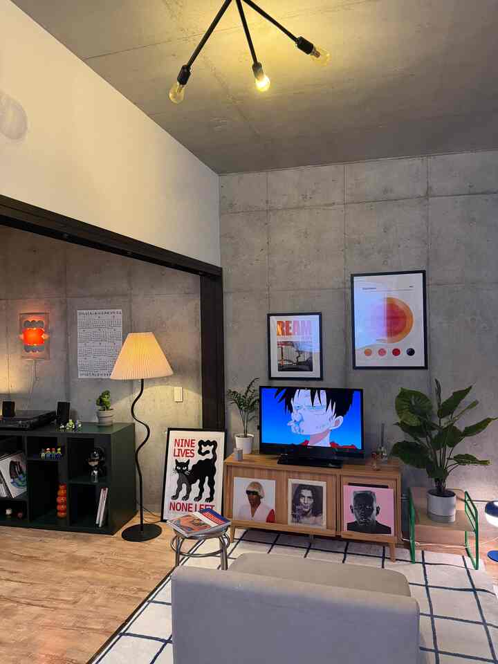 ナチュラルトーンのリビング、木製テレビ台と複数のポスター、フロアランプが配置されたモダンなインテリア