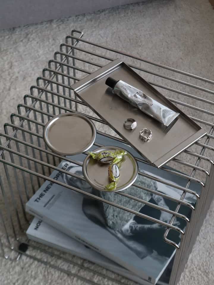 Modern interior accessory setup featuring a silver metal wire shelf with stainless steel trays and small items arranged neatly