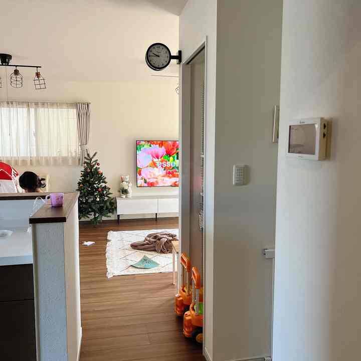 ブラウンの木目床と白い壁のリビングとキッチン空間、子供のおもちゃと時計が配置された雰囲気のあるインテリア