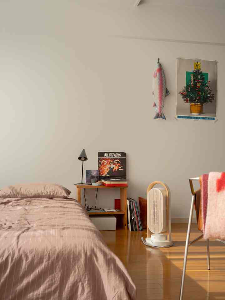 白い壁と木目調の寝室、暖かい寝具とセラミックヒーターが配置された居心地の良い一人暮らしのワンルーム