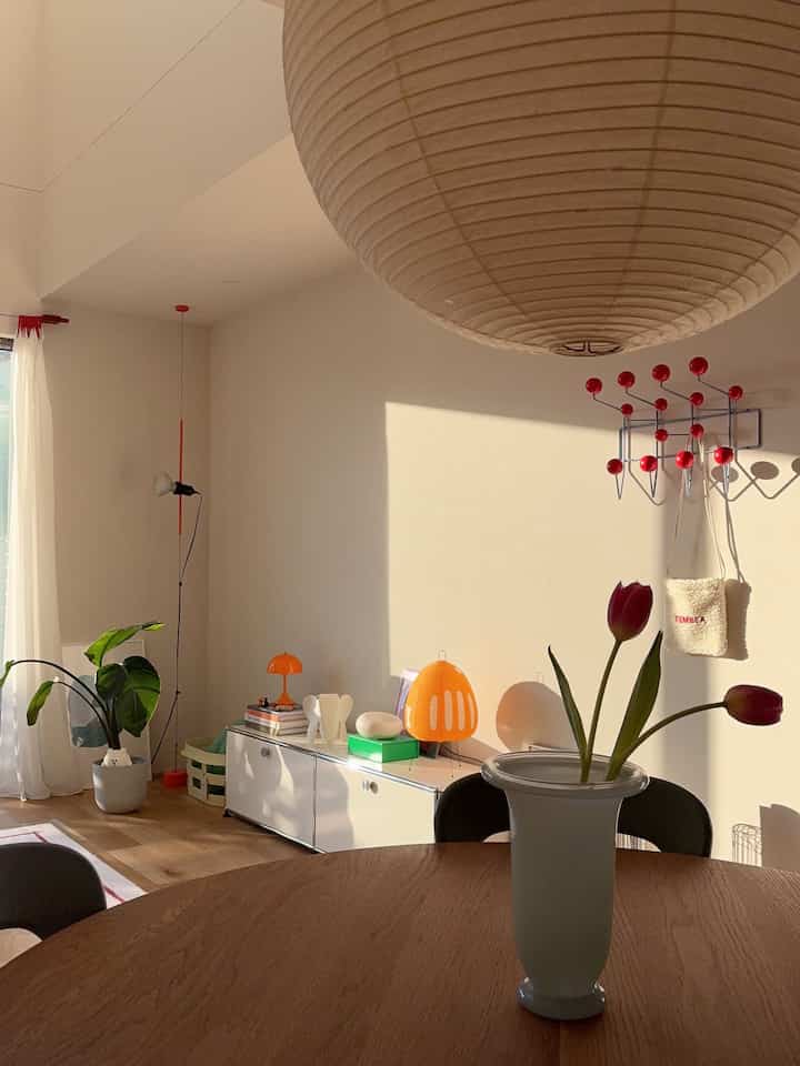 A cozy living space with soft light brown and natural tones, featuring a wooden dining table, coat rack, and potted plant