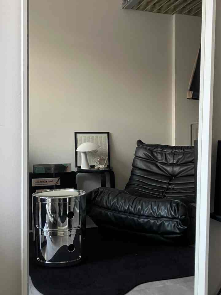 Modern and minimal living room featuring a black leather armchair, silver drawer unit, and white table lamp as accent