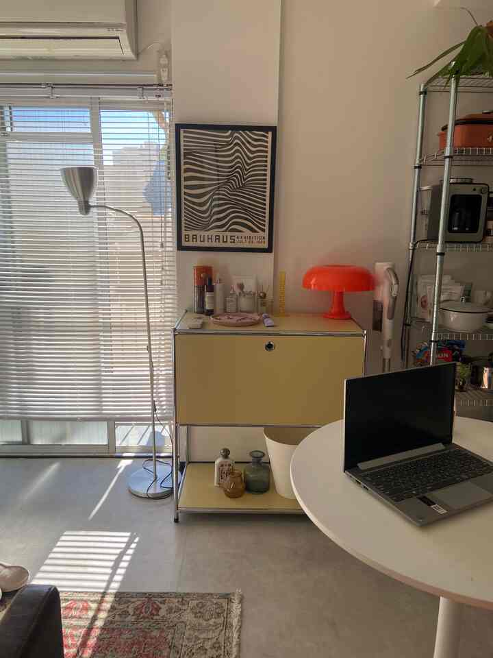 ホワイトとイエローのトーンの1DKリビング、丸テーブルの上にノートパソコンと窓辺にフロアランプが配置されたモダンな空間