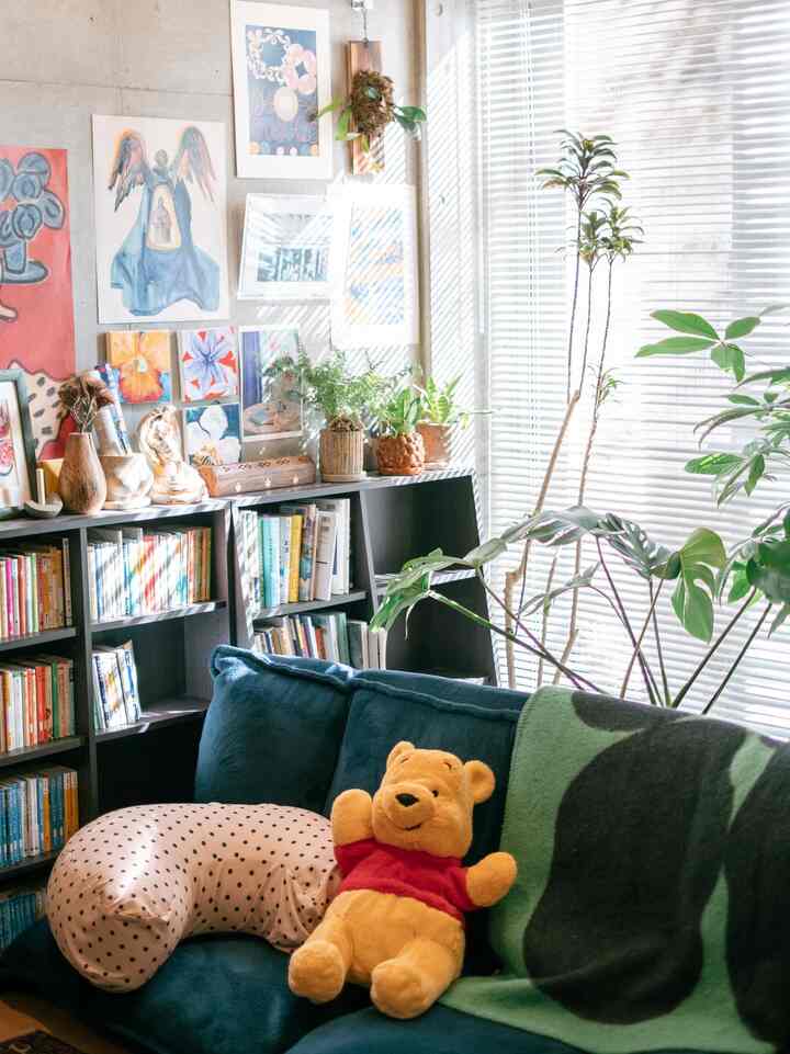 白と青の色調のリビング、ソファと本棚が配置され、多くの植物とウォールアートで雰囲気のあるインテリア