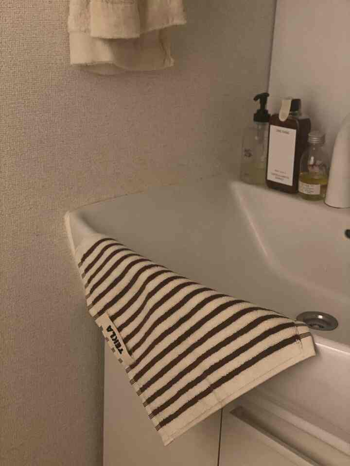 白い洗面台に茶色のストライプのテリーゲストタオルが掛けられ、整頓された浴室用品が並ぶ雰囲気のあるインテリア