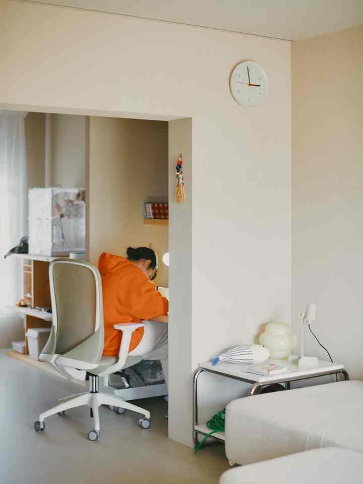 ベージュとホワイトの色調のワンルーム、リビング兼ホームオフィスの空間で、シンプルでナチュラルな雰囲気のデスクとオフィスチェアが配置されたインテリア