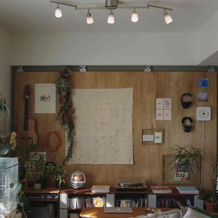ナチュラルな木目調の壁に複数の額縁、植物、レコードプレーヤーが配された二人暮らし向けのリビングインテリア