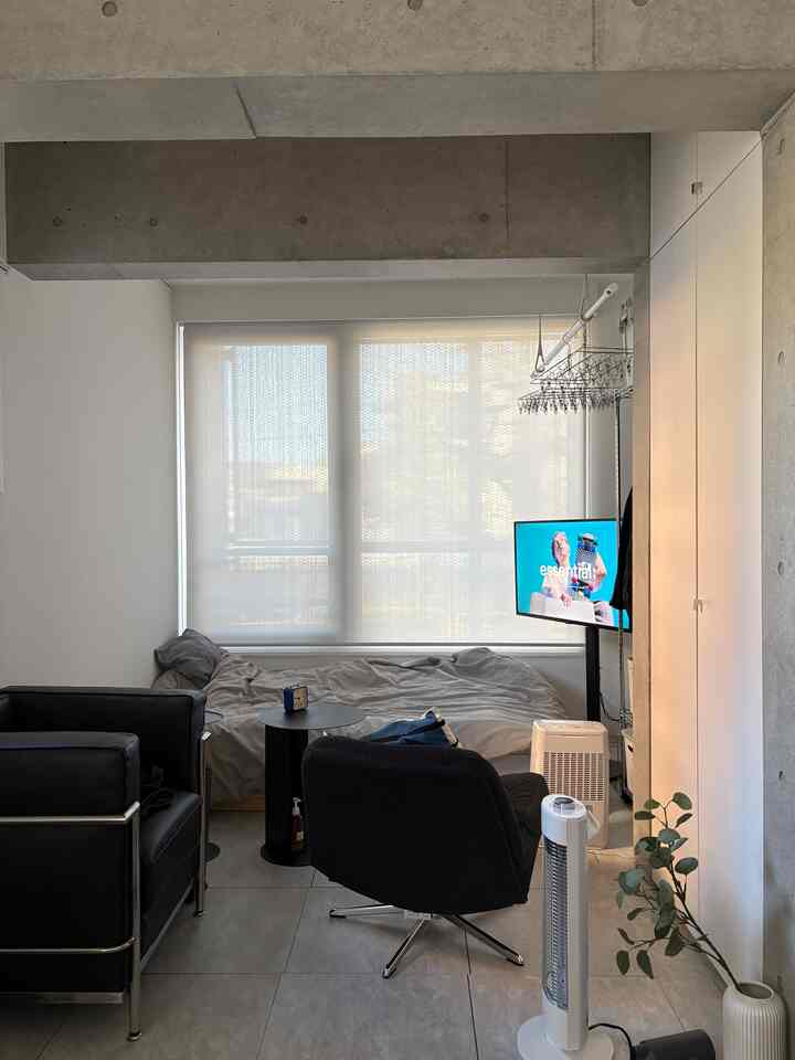 Monotone studio apartment bedroom and living space featuring black armchairs and a small side table with a simple interior design