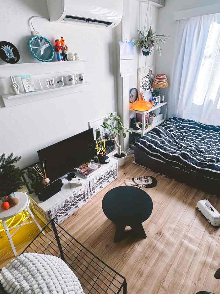 Bright natural-tone small bedroom featuring bed, desk with monitor, and round black table